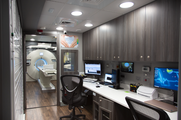 A PET Scan machine and computers with chairs in front of them inside a mobile Cardiac Imaging clinic.