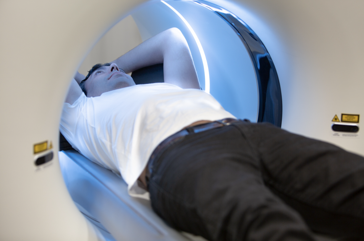 Man in white shirt and black pants lying down inside a PET Scan machine.